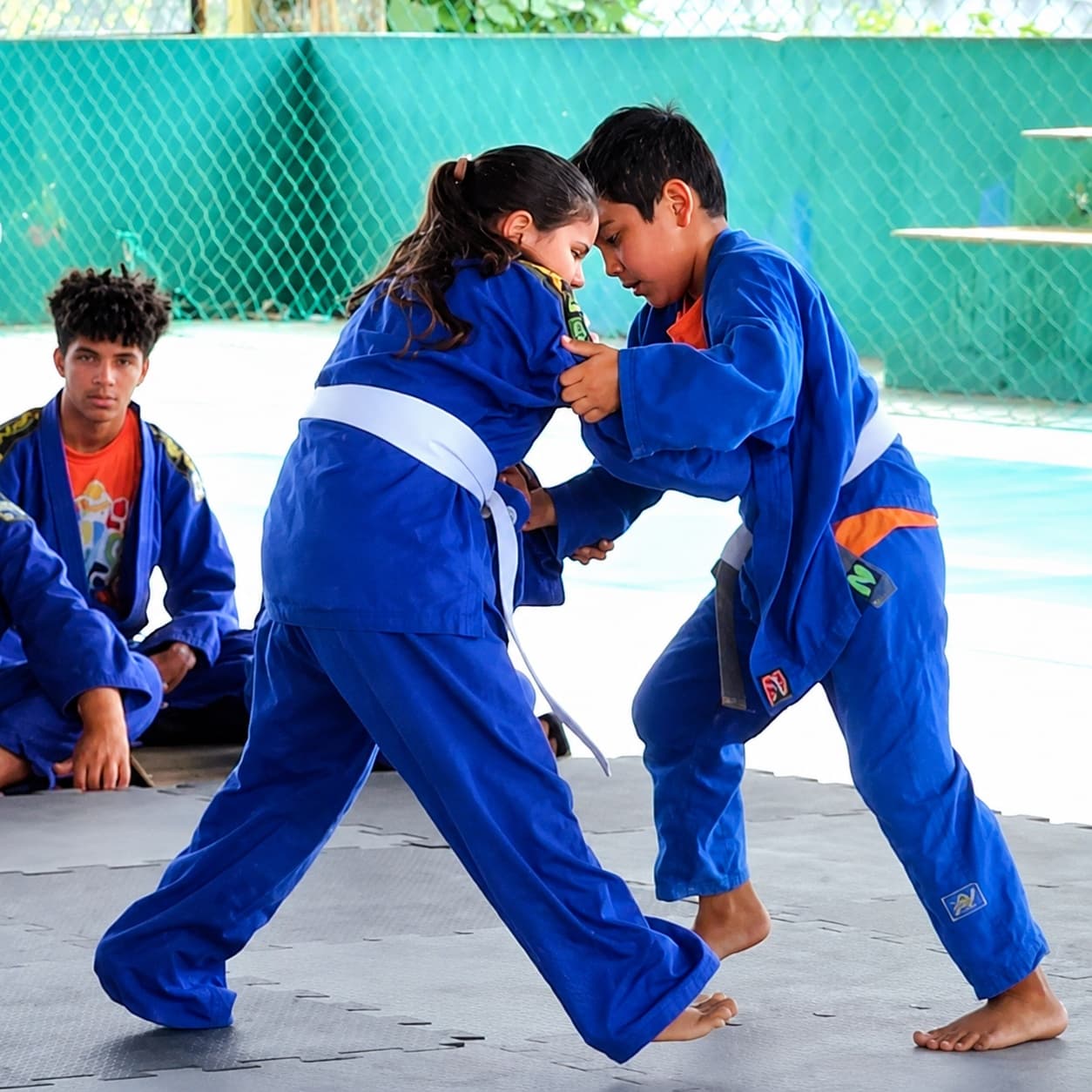 Dois jovens do FFC Esportes treinam judô de kimono azul no tatame.