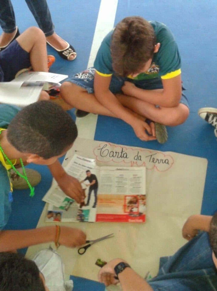 Jovens recortam revistas na oficina "Carta da Terra" durante atividade do grupo.