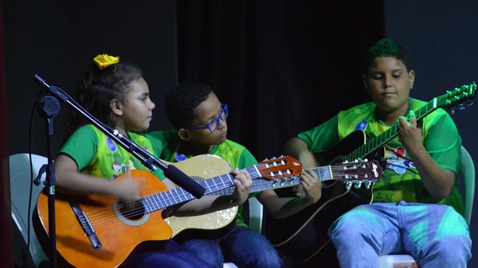 Jovens participam de uma oficina de música e tocam violão no palco